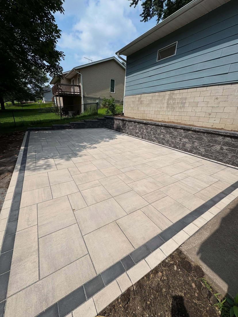 Newly installed stone patio with sleek tiles next to a house and a landscaped garden.